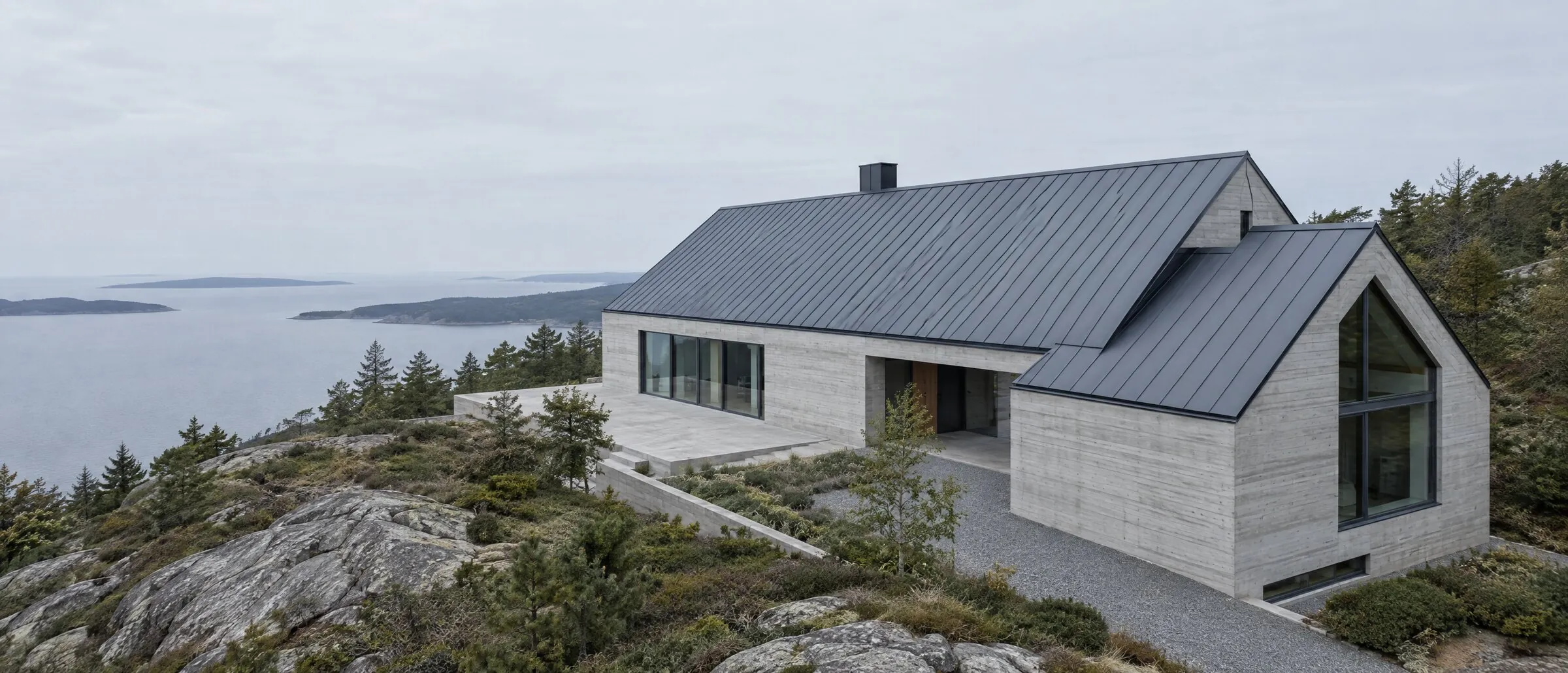 A long concrete house with a dark standing-seam steel roof, on rock above the sea.