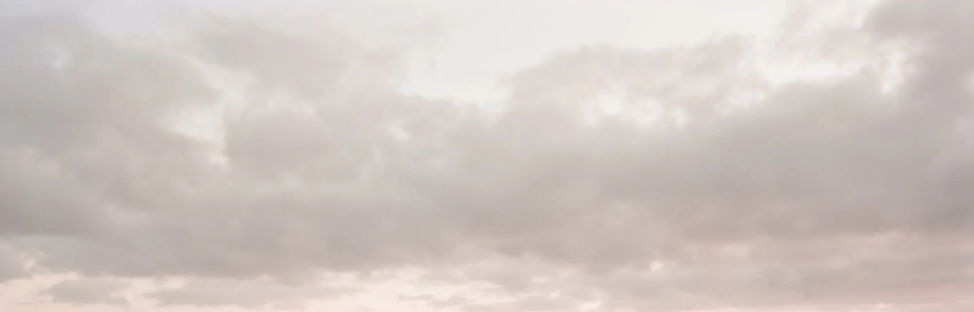A wide, pale evening sky, cloud turning rose at the horizon.
