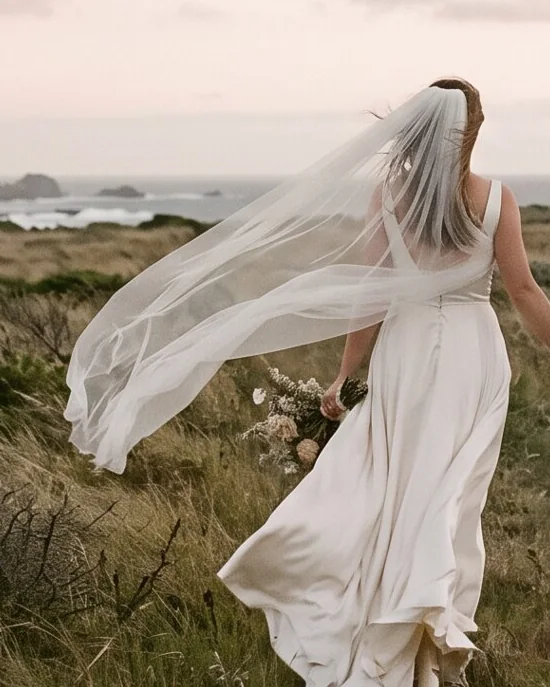 The bride mid-step, veil and dress lifted by the wind.