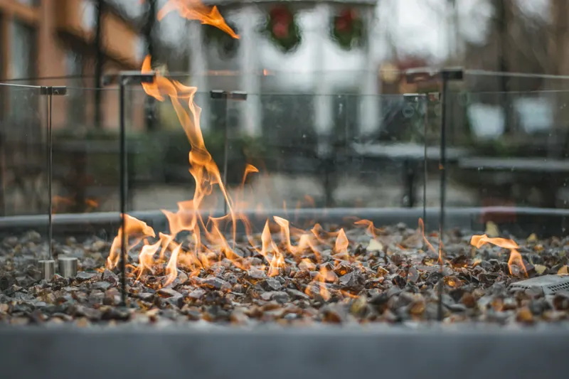 Flames over the glass and stone of an outdoor fire table at dusk.