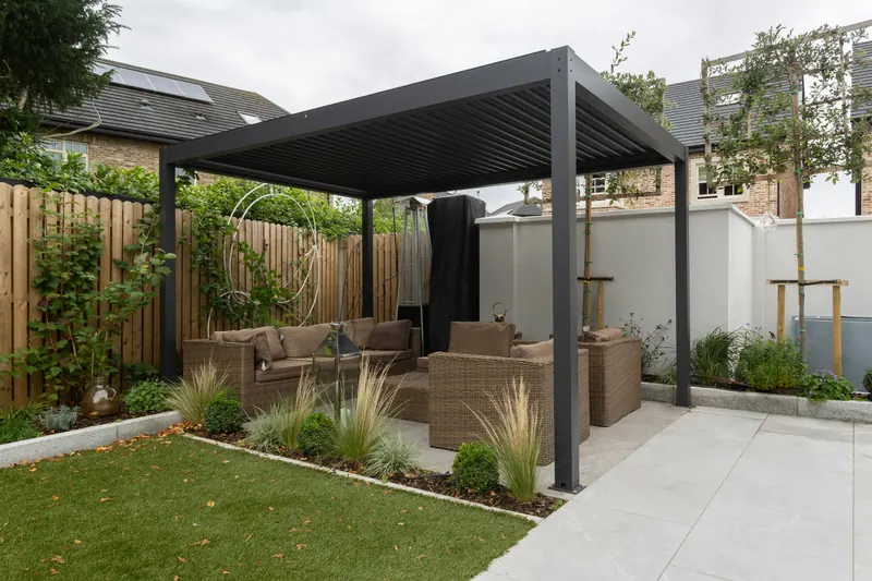 Contemporary Stone Patio: Large-format paving, a louvred pergola and a planted edge make a small yard feel generous.
